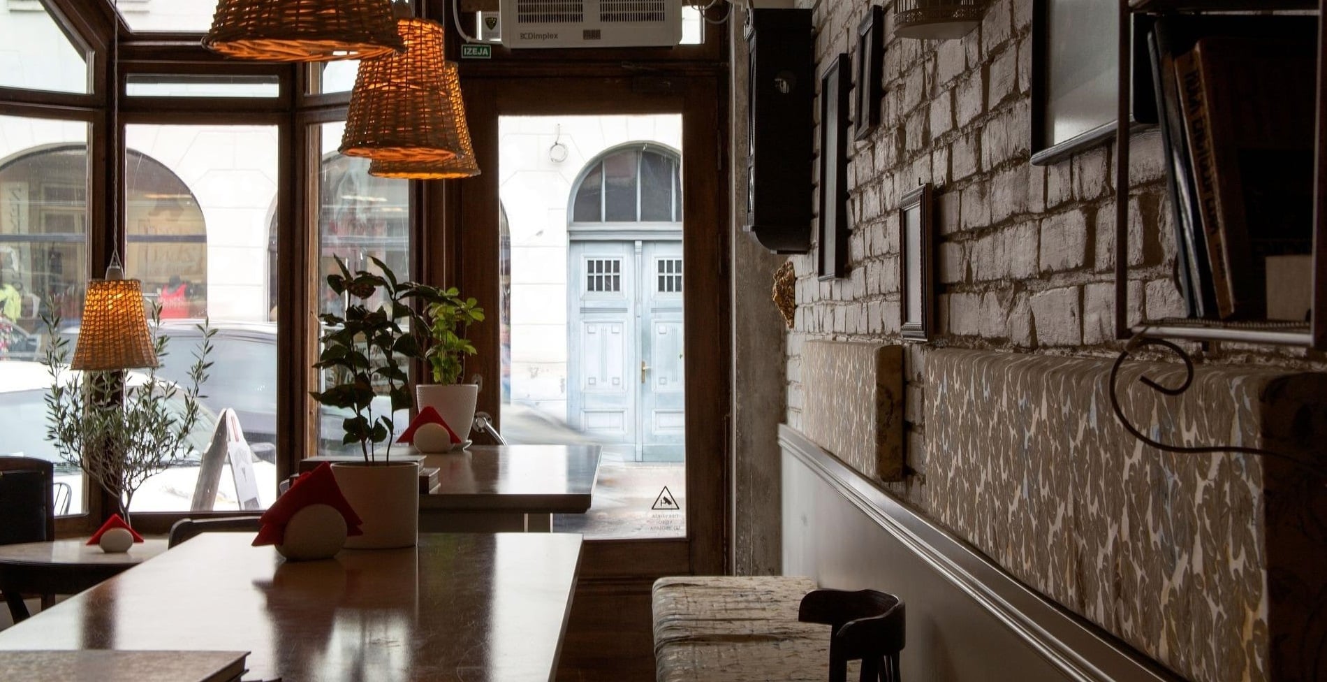 カフェもしくはレストランを想起させる欧風な店舗内観（テーブル、照明、観葉植物、レンガの壁）および店内から窓外風景も見える写真
